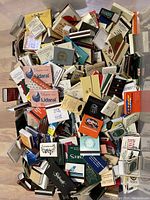 Pile of assorted vintage and international matchbooks viewed from above, showing a variety of logos, colors, and advertising designs.