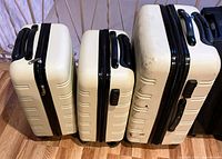 Three pale yellow/white hard-shell suitcases with black accents, showing wear and scuff marks, arranged side by side on a wooden floor.