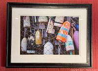 Framed photograph of colorful fishing buoys behind a wire net, black frame with white mat