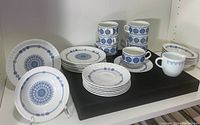 Full set arranged on black cloth display, showing cups, saucers, bowls, plates, and creamer, all featuring blue Granada Castillian pattern on white ironstone.