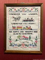 Photo of framed hand-made sampler showing airplane, ship, train, house and embroidered text with personalized details.