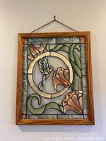 Frontal photo of stained glass art featuring a hummingbird and flowers in wood frame hanging on a wall