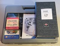 Gray plastic carrying case containing the new kid's microscope set, showing the label for the 52-piece set and a box of vintage Propper Bev-I-edge micro slides next to a black and white checkered box.