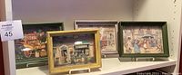 Four vintage shadow boxes on display shelf, showing varied colored frames and intricate three-dimensional street scenes.