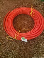 Coiled orange PEX tubing tied with yellow string sitting on gravel ground.