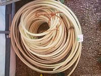 Coiled white PEX tubing, diameter 5/8 inch, tied with orange rope, placed on gravel ground