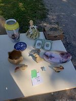 Full lot displayed on table outdoors showing all items including vase, Delft plate, figurine, floral trays, wooden box, decorative birds, ceramic planter, and oval floral dish