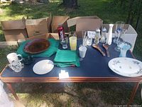 Full display of the lot on a table outdoors including assorted glasses, plates, placemats, mugs, salt and pepper shakers, and utensils.