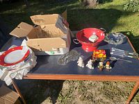 Overview of assorted kitchen items on table showing plates, salt and pepper shakers, glass coasters, colander, and miscellaneous small items