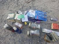 Overview of lot showing assorted hardware and kitchen-related items scattered on ground including bulbs, spray cans, glass jars, and hardware boxes