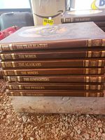 Stack of vintage hardcover books with brown covers from the 1970s, showing titles such as The Trail Blazers, The Women, The Alaskans, The Miners, The Gunfighters, The Pioneers, and The Loggers