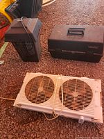 Photo showing the bug zapper, window fan, and closed toolbox arranged together on a gravel surface.
