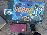 Scene It? DVD movie trivia game box, a small boxed item and part of a shoe visible on ground