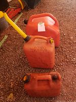 Three orange plastic gas cans of various sizes with caps and one spout, placed on the ground
