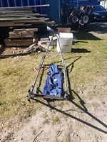 Folded foldable metal frame hammock stand with a blue carrying bag on grass outdoors.