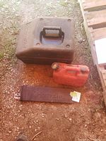 Black Homelite carrying case, red gas can, and Homelite chainsaw bar protective cover on the ground