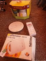 Philips waffle maker box next to round marble Lazy Susan and plastic ice cube tray on gravel floor.