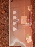 Photo of the boxed 4 light vanity fixture showing four clear glass shades mounted on a gold finish bar with bulbs included inside the box.