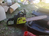 Overall view of the Poulan chainsaw alongside the carrying case and gas can on grass ground.