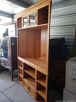 Full view of red oak corner TV unit showing open shelves, upper glass-paneled cabinet doors, and lower cupboards with doors.