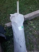 White storage bag holding folded fabric sun shade lying on grass.