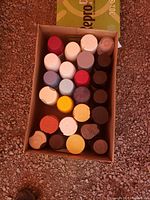 Top view showing open box containing 22 spray paint cans in various colors including yellow, white, red, brown, black, and gray.
