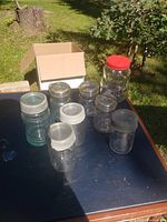 Nine mason jars on table including a large bear-shaped jar with red lid, others with silver metal lids and various sizes; all clear glass.