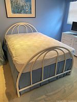 Full view of the white metal bed frame with mattress, mattress cover, and blue bedskirt in a blue room, showing headboard and footboard design.