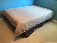 Side view of full-size bed with beige duvet cover and dark brown bed skirt, showing bedding condition and appearance.