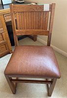 Front view of the wood chair showing brown vinyl padded seat and vertical slatted backrest.