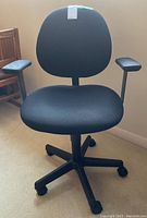 Front view of black office chair with fabric seat and backrest, armrests, and black plastic five-prong rolling base.