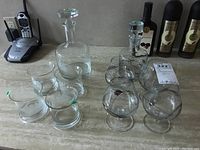 Photo showing both decanters, four snifter glasses with silver overlay, and four matching etched ship motif glasses on a countertop with bottles in the background.