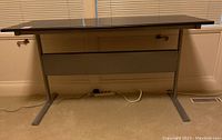 Front view showing the dark stained wood top, metal base, drawer with lock, and power cord on floor.