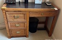 Photo of the wooden desk showing front and left side with three drawers and dark top surface