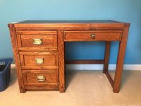 Front view of oak wood desk with three drawers on left and central drawer, black leather top.
