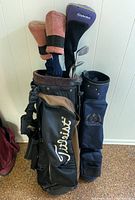 Full frontal view of Titleist golf bag with clubs including TaylorMade headcovers and socks, next to smaller blue golf bag