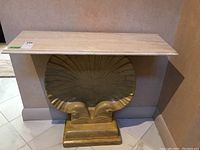 Front and angled view of console table with travertine marble top and gold resin seashell base on a beige tile floor.