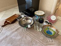 Overview of collected kitchenware showing stainless steel bowls, glass bowls, clear ramekins, ceramic teapots, wooden trays, and other items arranged on a towel on the floor.