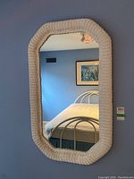 Front view of wall mirror showing white wicker frame and reflection of bed and blue wall.