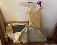 Four framed items wrapped partially in brown paper and bubble wrap leaning against a white wall on the floor.