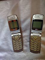 Two silver LG flip phones open, showing small monochrome screens and numerical keypads.