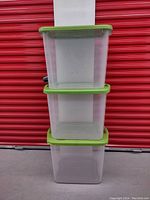 3 large clear plastic tote bins stacked with green lids, showing general size and condition