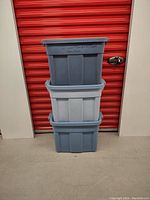 Stack of 3 Rubbermaid Roughneck tote bins in front of a red storage unit door, showing color and general size.