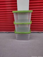 Front view of three stacked clear plastic Sterilite bins with green lids showing minor wear and some writing on lids.
