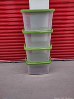 Four Sterilite medium-sized translucent plastic tote bins stacked, showing green lids and no visible damage.