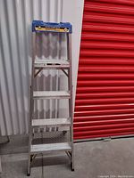 Front view of the 5 foot aluminum step ladder showing 5 wide steps and blue top cap with warning labels.