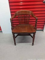 Front view of antique wooden chair showing curved backrest, vertical slats, armrests, and turned legs.