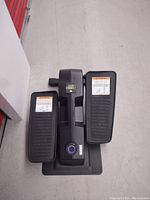 Overall view of the black Cubii compact elliptical with foot pedals and digital display, placed on a concrete floor.