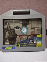 Grey plastic case with clear window showcasing microscope and accessories inside.