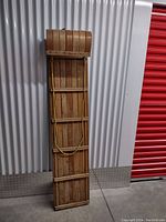 Full view of the long rectangular wooden sled standing upright showing slatted base and rope tied around middle